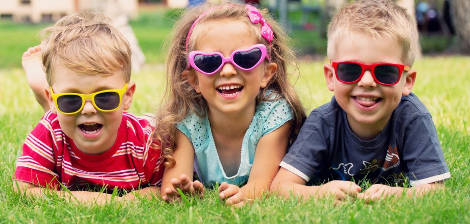 3 Kinder liegend im grünen Rasen 